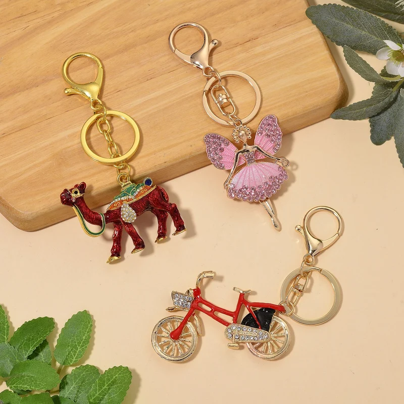 3er-Set emaillierte weiße, schwarze und rosa Kristall-Schlüsselanhänger mit Fahrrad, Kamel und geflügelter Ballerina, Legierung in Gelbgold